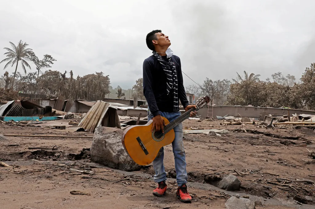 Brian Rivera, který ztratil na následky sopečné katastrofy v Guatemale 13 členů své rodiny, drží kytaru své sestry uprostřed zaprášených ruin rodného domu.