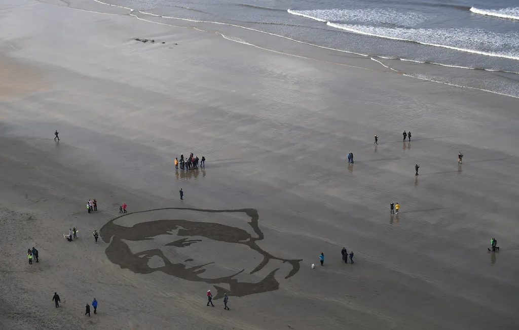 Lidé se scházejí během Dne příměří kolem pískové kresby portrétu armádní sestry Rachel Fergusonové, která zemřela v červnu 1918 během první světové války. Pláž Downhill Beach ve městě Coleraine, Severní Irsko