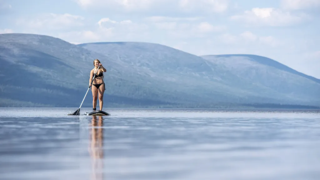Žena na paddleboardu na jezeře Pallasjarvi. To se nachází v laponské části Finska nad severním polárním kruhem
