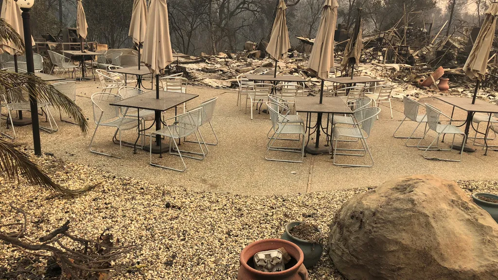 Stoly venkovní kavárny a slunečníky, které zůstaly na terase podniku Mama Celeste's Gastropub po požáru ve městě Paradise