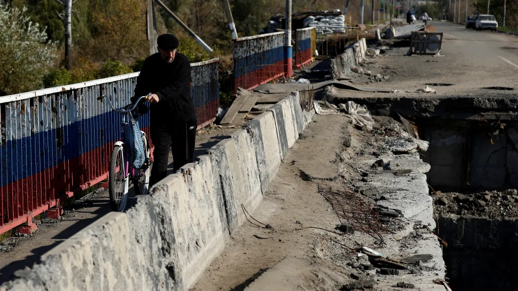 Muž přechází rozbombardovaný most v Kupjansku