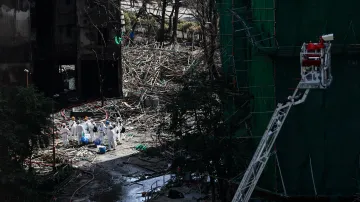 Záchranáři v ochranných oblecích stojí mezi budovami bytového komplexu v Hongkongu, zničenými požárem