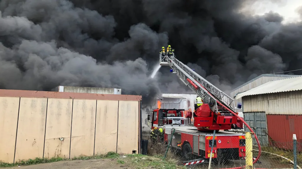 Hasiči krotí plameny stoupající z haly v Písnici