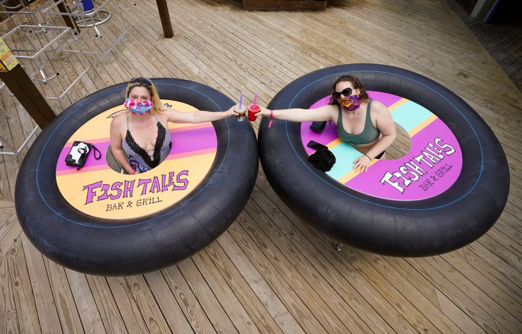Tracy a Julie pózují s drinky u "bumper tables", stolů s nárazníkem. Stolky mají kolečka, aby se hosté mohli v bezpečné vzdálenosti volně pohybovat po podniku Fish Tales Bar & Grill v Ocean City v americkém Marylandu