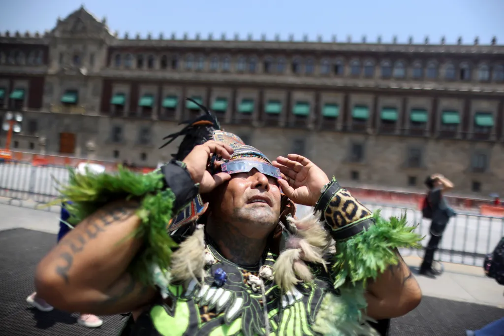 Muž oblečený jako aztécký tanečník pozoruje částečné zatmění Slunce v Mexico City