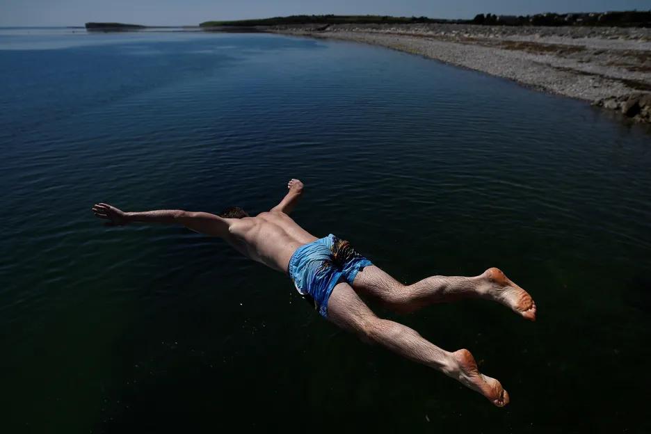 Muž při skoku do moře na pláži Salthill za slunného dne v irském městě Galway