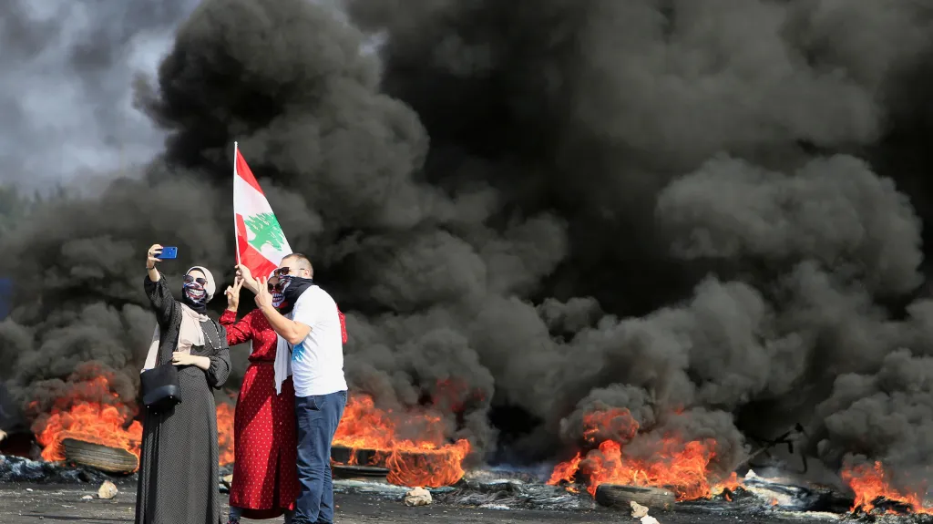 Demonstranti si fotí selfie před zapálenými pneumatikami v Bejrútu