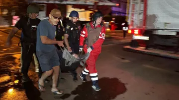 Záchranáři a dobrovolníci vynášejí osobu evakuovanou z bytového domu