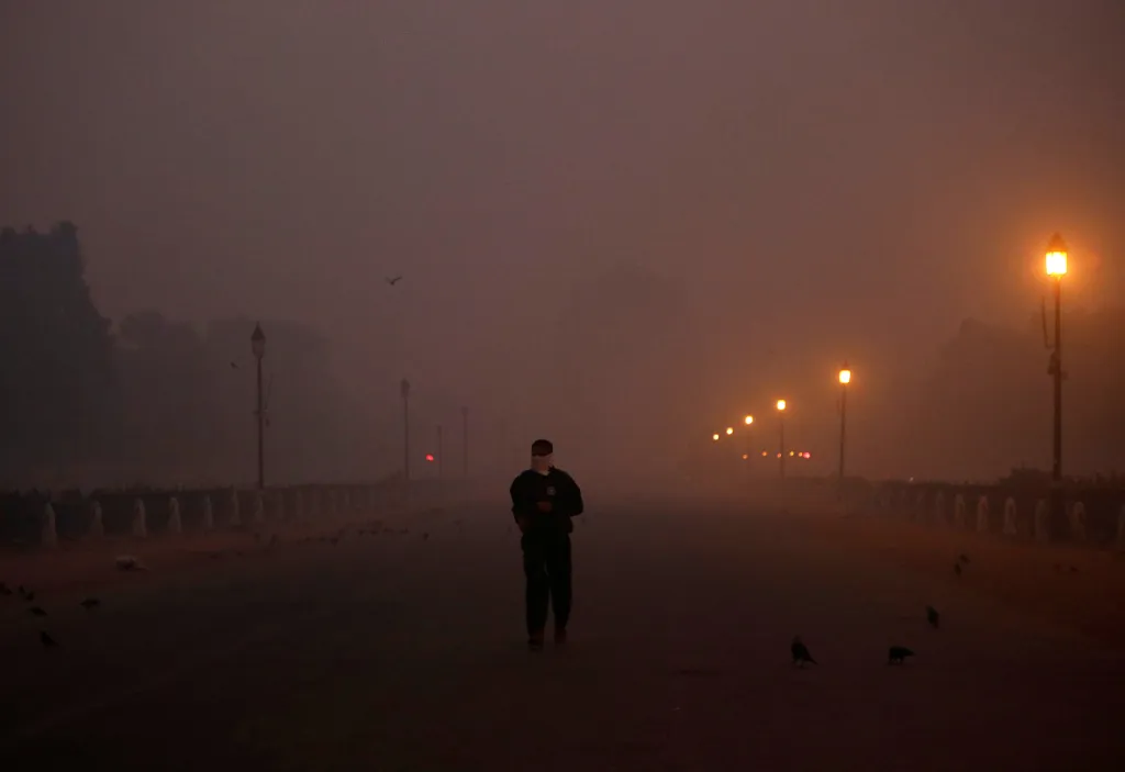 Muž se zakrytou tváří před válečným památníkem India Gate za brzkého rána a hustého smogu v Novém Dillí.
