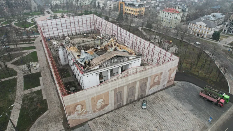 Mariupolské divadlo zničené ruským útokem zakrývala během demolice trosek a stavby nové budovy zástěna (prosinec 2022)