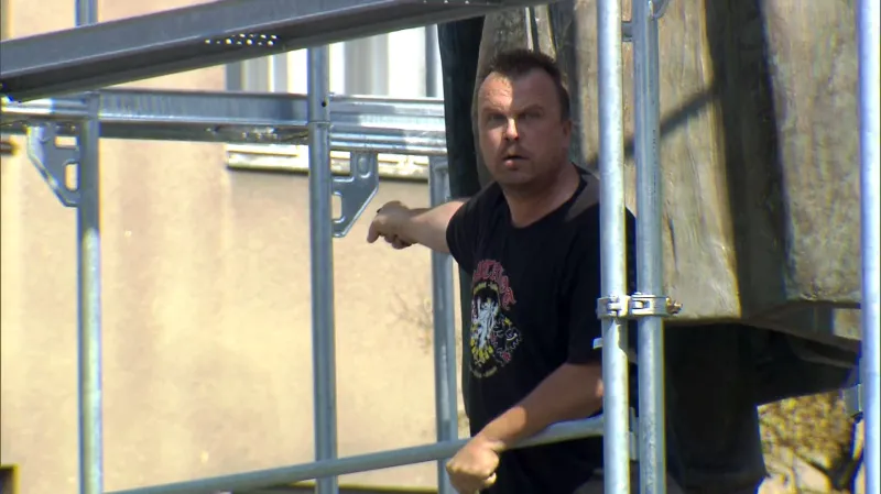 Muž, který sundal s plachtu z lešení kolem sochy maršála Koněva