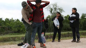 Americký pohraniční strážník prohledává migranty při jejich pokusu o ilegální přechod hranic z Mexika do USA v údolí Rio Grande