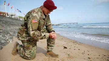 Americký voják na pláži Omaha drží v ruce písek, na kterém prolívali krev jeho předchůdci