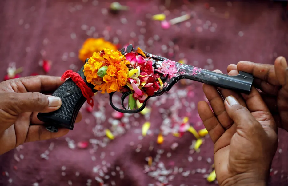 Policista drží revolver ozdobený květinami během modlitby v rámci hinduistické slavnosti Dussehra v indickém Ahmadábádu