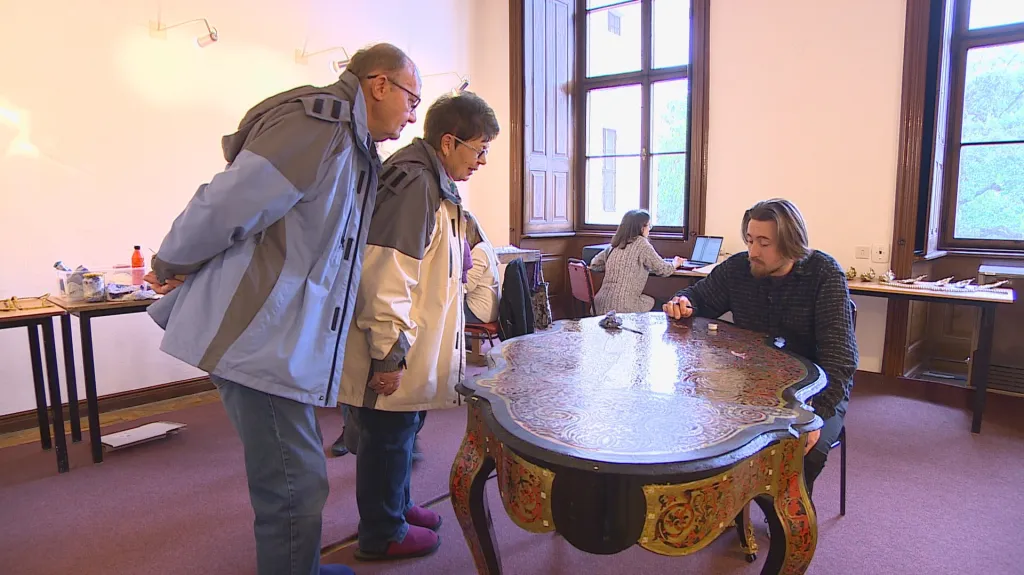 Návštěvníci zámku sledují restaurátora při práci
