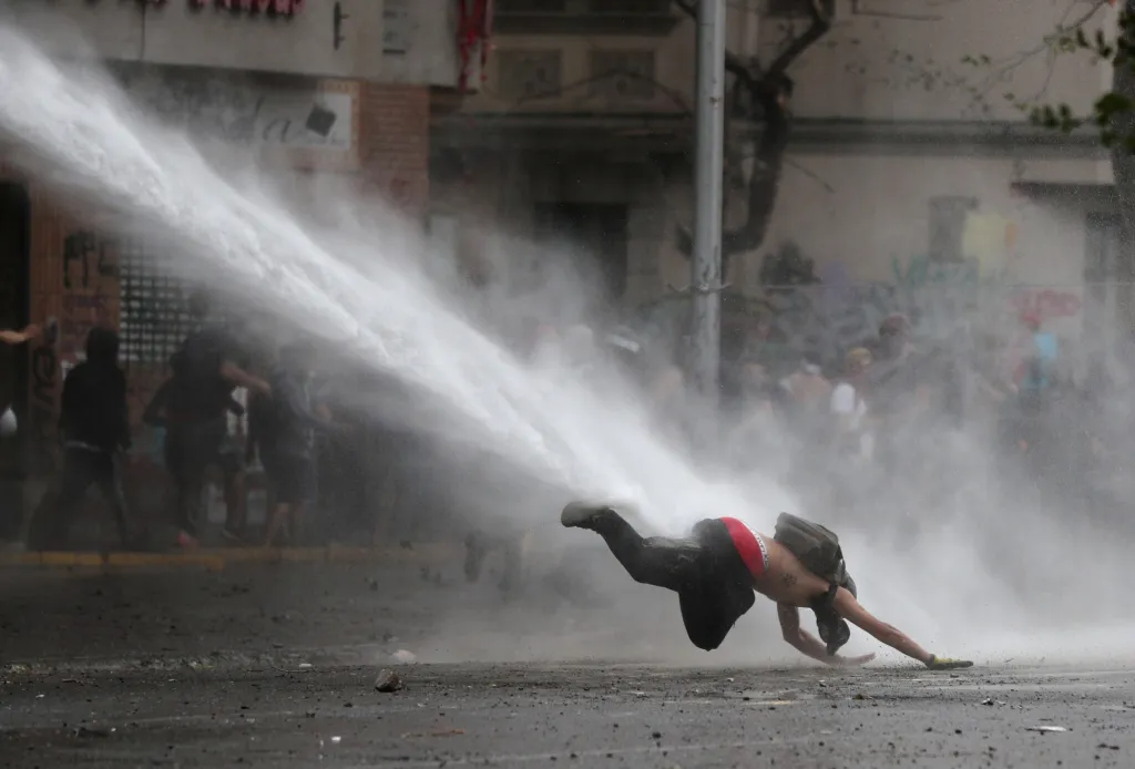 Jeden z protestujích je sražen vodním dělem během protivládních protestů v chilském Santiagu