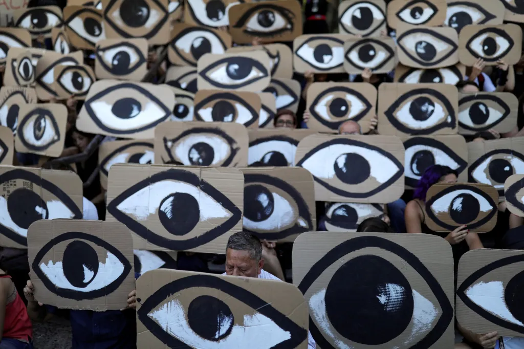 Demonstranti drží transparenty během protestu proti chilské vládě. Upozorňují na to, že „oko“ vidí všechny kroky, které vláda dělá proti zájmům veřejnosti. 10. prosince 2019 v Santiagu v Chile