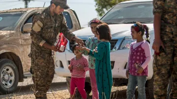 Příslušník kurdské milice rozdává sladkosti dětem v Tall Abjadu