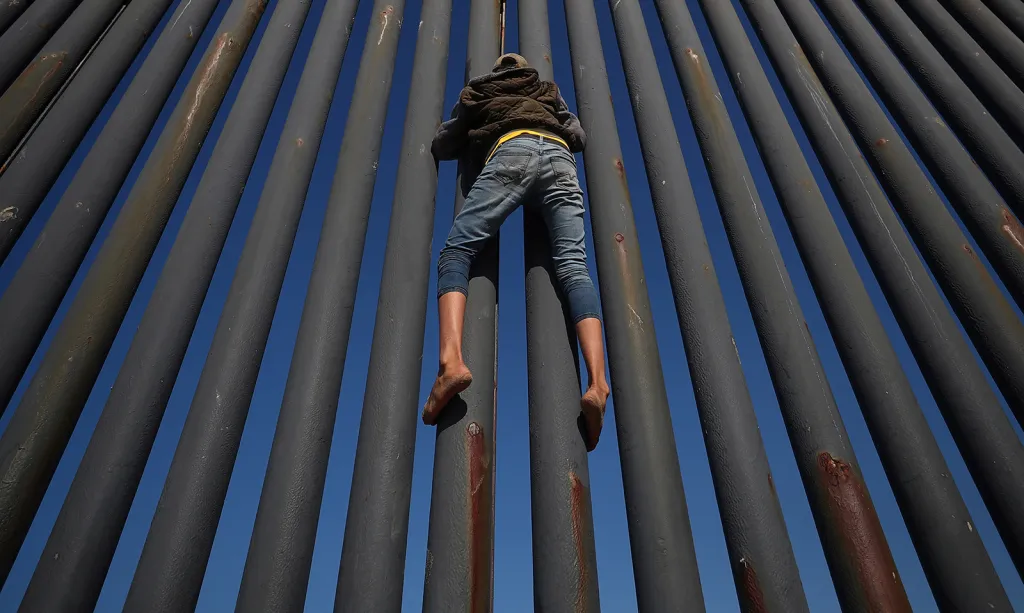 Migrant ve snaze vyšplhat se na hraniční plot mezi Mexikem a Spojenými státy ve městě Tijuana.