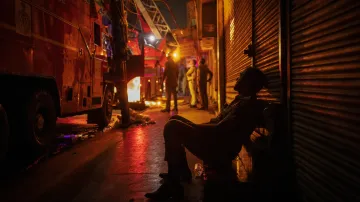 Vyčerpaný hasič sedí vedle hasičského vozu během probíhajícího požáru v několika obchodech s textilem (13. června 2024)