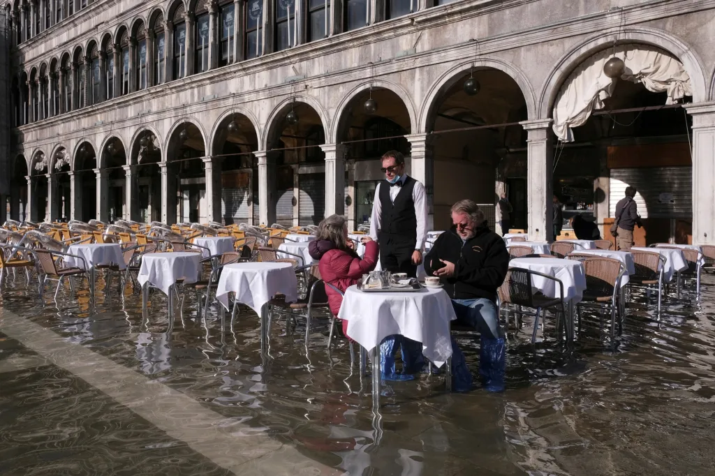 Lidé sedí v kavárně na zaplaveném náměstí svatého Marka během zvýšené hladiny moře, které se v pátek rozlilo po Benátkách