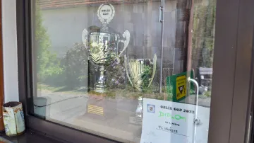 Výloha obchodu je zaplněná trofejemi, které místní fotbalový tým získal po triumfu v letošním Orlík Cupu. První místo získal porážkou šesti týmů z okolí