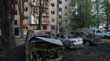Pohled na auta a obytný dům poškozený náletem ruského dronu