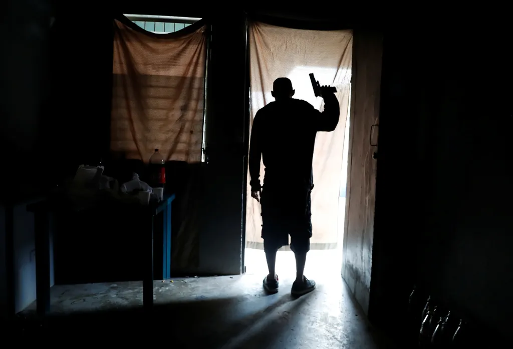 Člen pouličního gangu MS-13 sleduje ze svého domu situaci na ulici, zatímco policejní hlídka prochází městem San Pedro Sula v Hondurasu. Muž byl zraněn během přestřelky mezi konkurenčními gangy MS-13 a Barrio 18 a později na následky zranění zemřel.