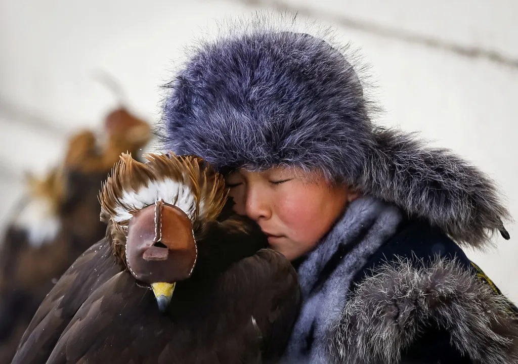 Mladý lovec odpočívá vedle svého ochočeného orla skalního během každoroční tradiční soutěže lovců v kazašském městě Almaty
