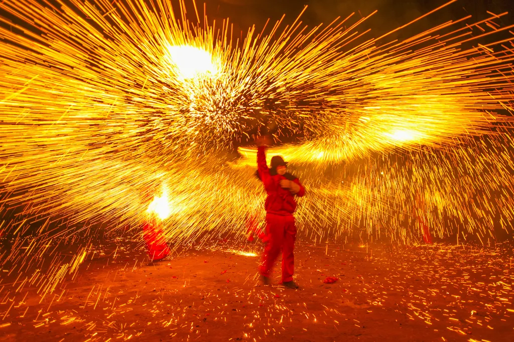 Pouliční performer předvádí sprchu jisker z roztaveného železa během oslav v průběhu Latern Festivalu v čínském městě Lu-čou