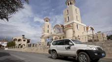 Auto OSN projíždí kolem kostela Agios Georgios v Pyle. Vlevo vyčnívá mešita