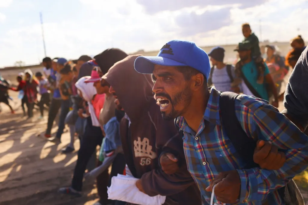 Lidé kráčí ruku v ruce vstříc příslušníkům mexického Národního institutu pro migraci (NIM)