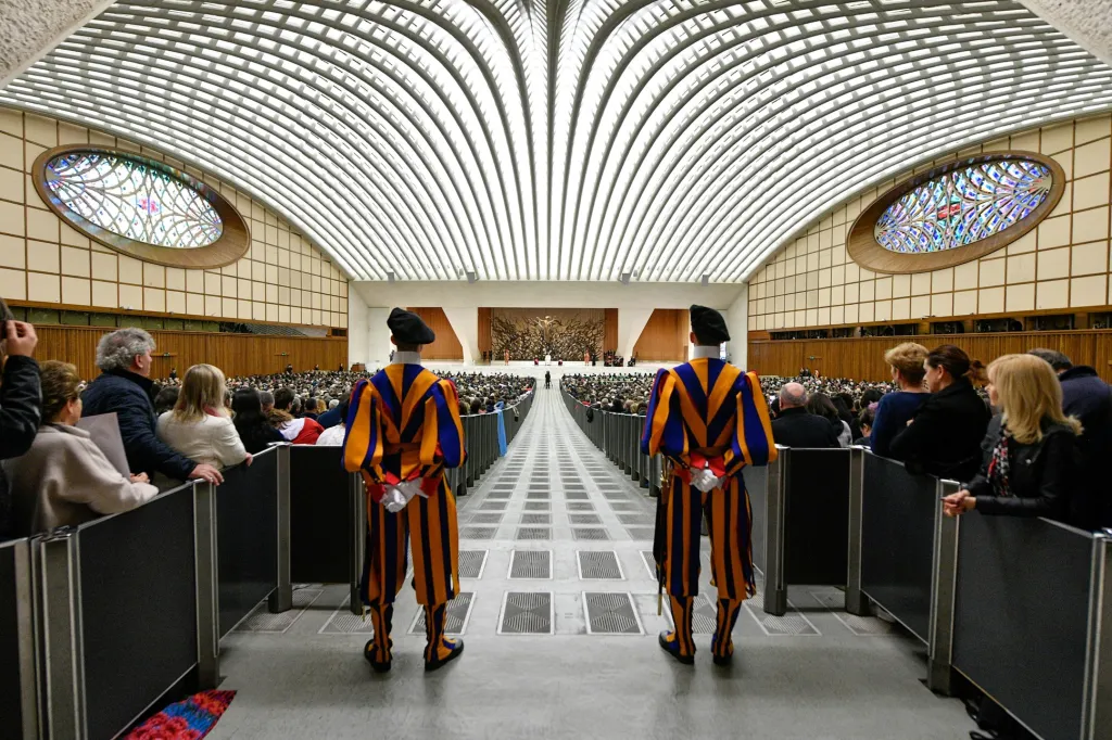 Příslušníci Švýcarské gardy stojí v popředí sálu ve Vatikánu, kde papež František pořádá pravidelné veřejné setkání