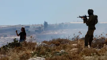Izraelský osadník (vlevo) natáčí palestinskou demonstraci, zatímco izraelský voják stojí na stráži (okupovaný Západní břeh, 9. června 2026)