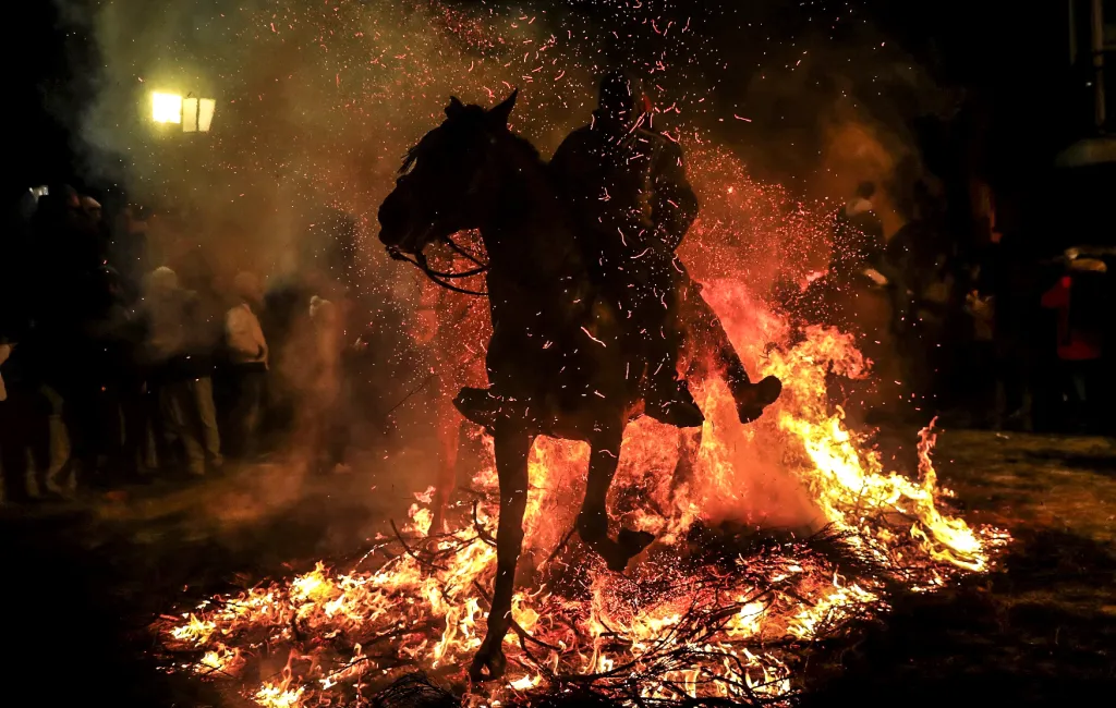 Jezdec na koni proskakuje plameny ohně z borovicových větví poté, co jeho koni požehnal kněz během kontroverzního festivalu Luminarias