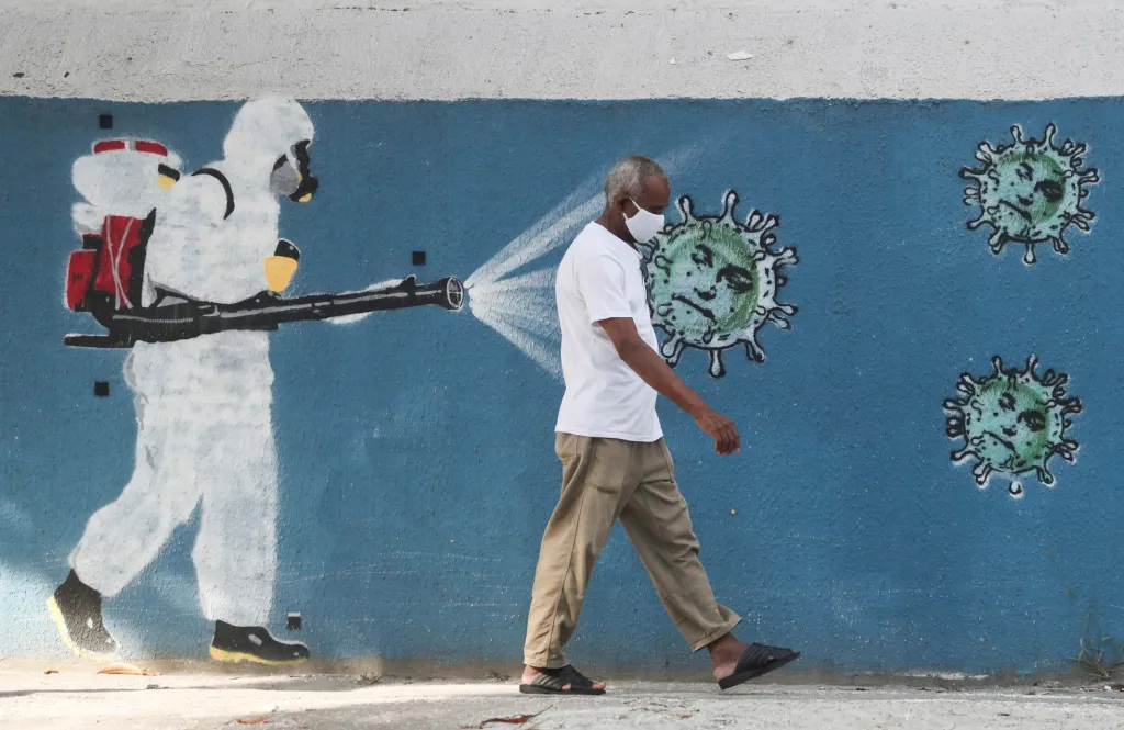 V Riu de Janeiro jde chodec vedle graffiti znázorňujícího zdravotníka, který ničí viry v podobě malých tváří brazilského prezidenta Jaira Bolsonara