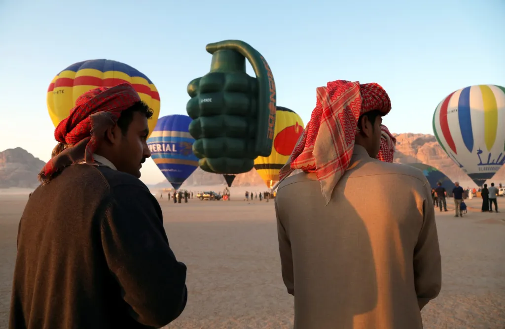 Muži sledují horkovzdušný balon ve tvaru granátu, který se stal součástí balonového festivalu v poušti Vádí Rum v Jordánsku