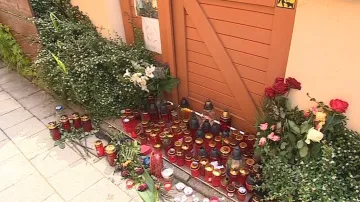 Před vchod do domu lidé stále pokládají květiny a svíčky
