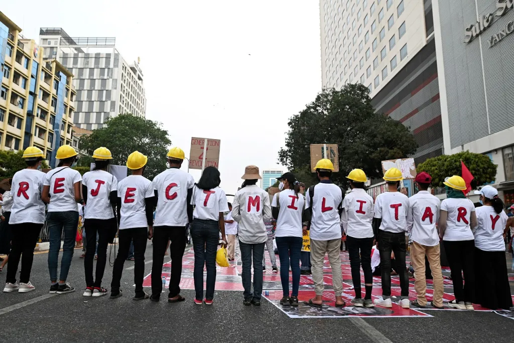 Demonstranti stojící v řadě vytvářejí díky písmenům na tričkách vzkaz „Reject Military“ (odmítáme armádu)
