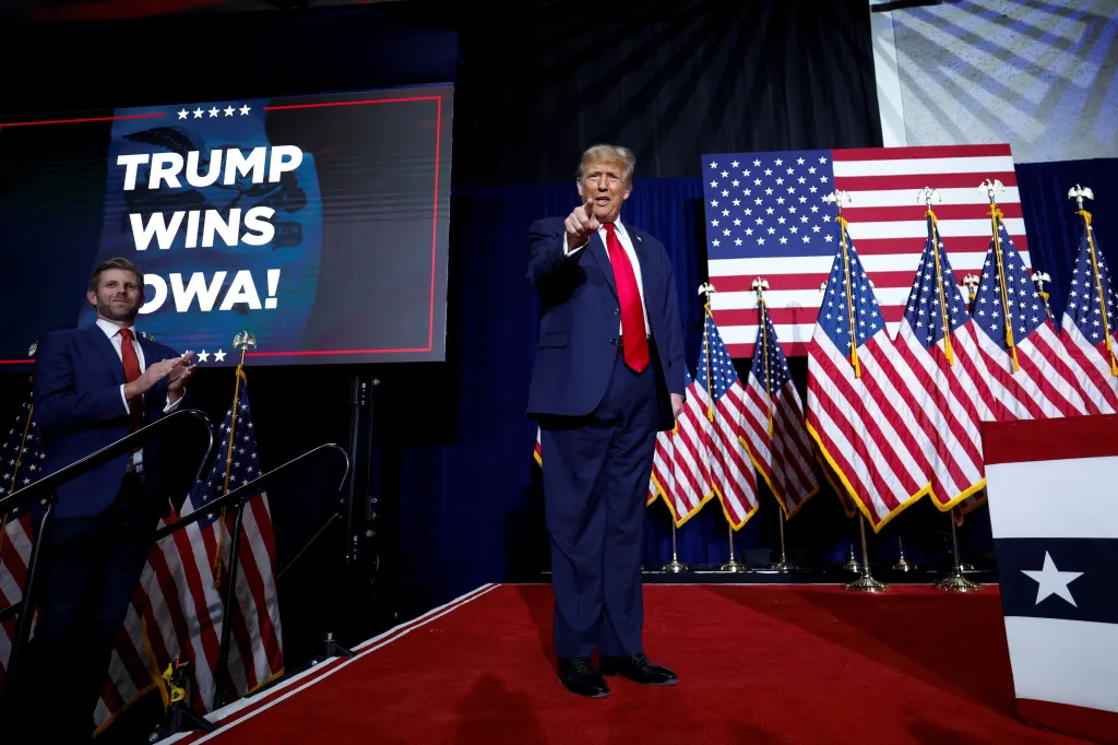 Donald Trump gestikuluje, zatímco jeho syn Eric Trump tleská vedle něj během noční volební párty v Iowě