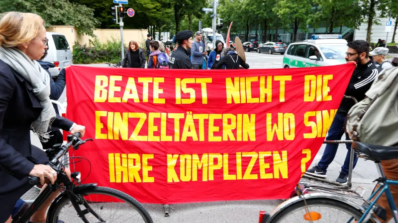 "Beate není jedinou pachatelkou. Kde jsou její komplicové?" ptá se jeden z plakátů před budovou soudu