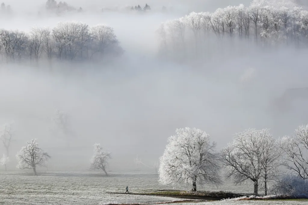 Švýcarsko se probudilo do nového roku v tichu a mrazu. Na snímku jeden z běžců probíhá zamrzlou krajinou poblíž průsmyku Albispass. 2. ledna 2020