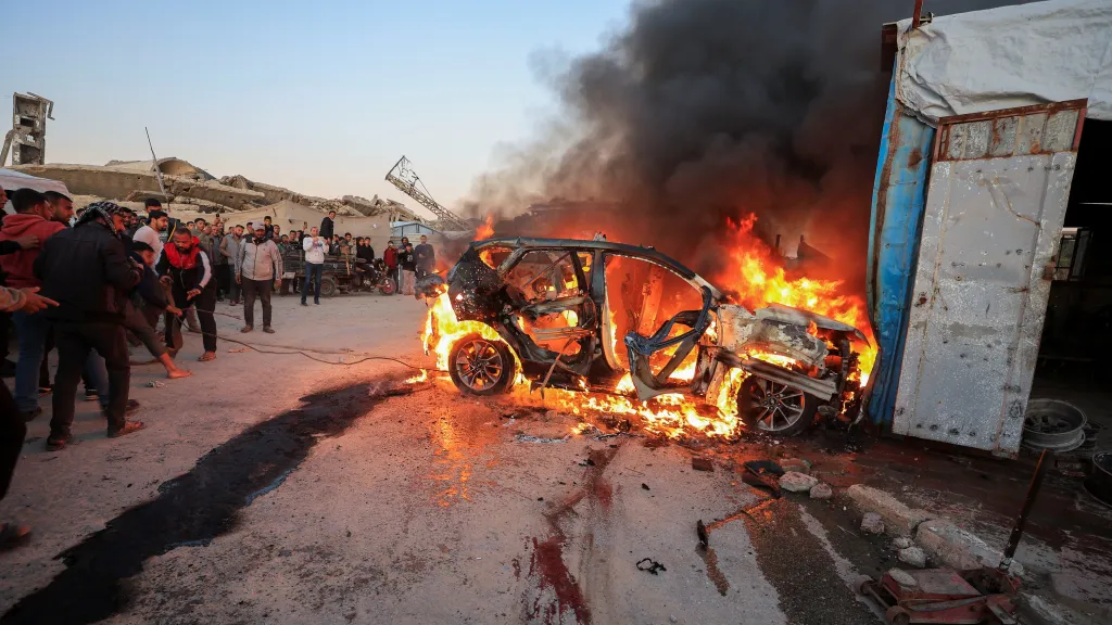 Lidé stojí poblíž hořícího vozidla po izraelském útoku, při kterém podle zdravotníků zahynul novinář stanice al-Džazíra Mohammad Wišáh