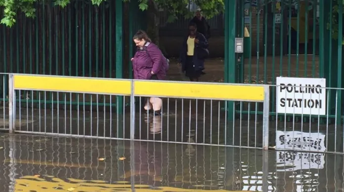 Žena se cestou z hlasování brodí po zaplaveném chodníku