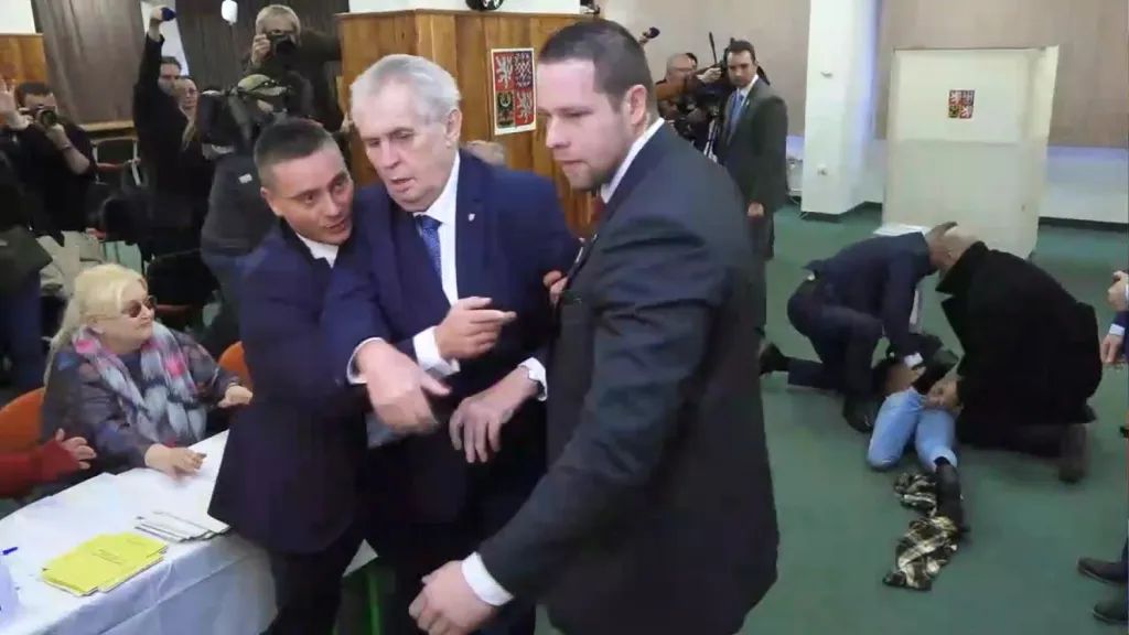 Ochranka zasahuje proti ženě, která se ve volební místnosti během prezidentských voleb polonahá vrhla směrem k prezidentovi Zemanovi při jeho hlasování 12. ledna 2018 v pražských Lužinách.