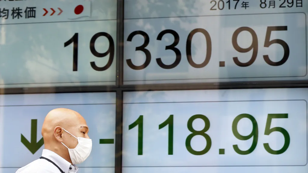 Muž prochází v Tokiu kolem elektronické tabule s akciovými indexy