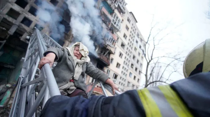 Záchranáři v Kyjevě pomáhají ženě opustit dům poškozený při ostřelování