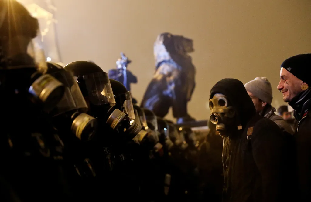 Demonstrant s plynovou maskou před kordonem policie během budapešťského protestu proti novému pracovnímu zákonu.