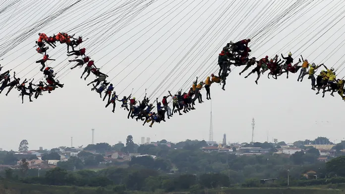 Lidé připoutaní lanem k mostu ve výšce 30 metrů se pokoušejí hromadným seskokem překonat světový rekord v této disciplíně. Hortolandia, Brazílie.