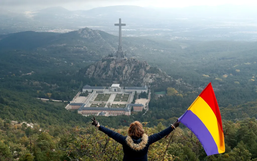 Španělsko se otevírá svojí historii a snaží se vypořádat s dědictvím své temnější stránky. Na snímku sympatizantka republikánů mává vlajkou v momentě, kdy se z údolí Valle de los Caídos (Údolí padlých) odvážejí ostatky diktátora Francisca Franca